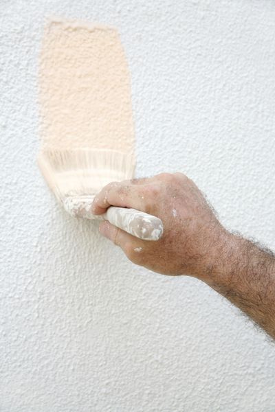 دست مردی که با رنگ پاشیده شده قلمویی در دست دارد و خانه ای را نقاشی می کند