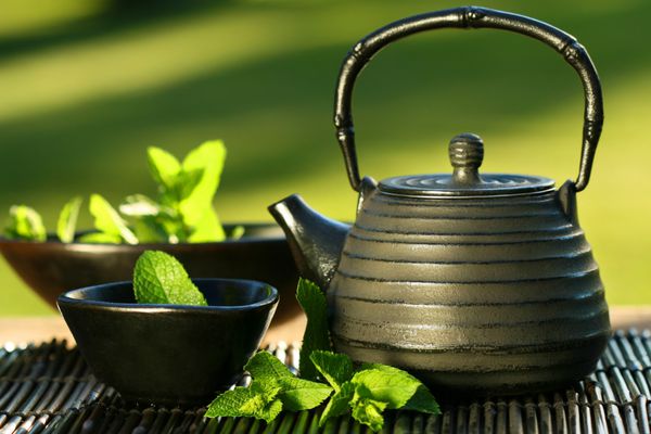 قوری سیاه آهنی آسیایی با شاخه های نعنا برای چای