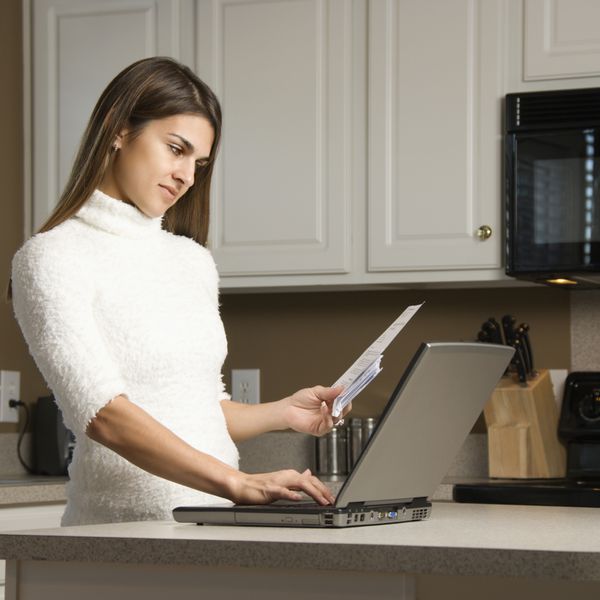زن قفقازی در آشپزخانه به کامپیوتر لپ تاپ نگاه می کند