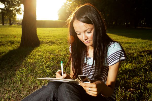 زن جوان زیبا در غروب آفتاب در فضای باز در پارکی می نویسد