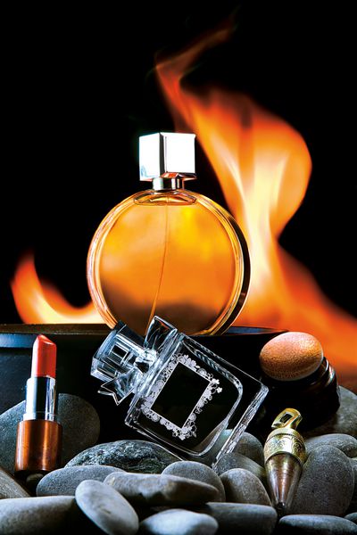 بوی شعله نمای نزدیک از دو بطری عطر و لوازم آرایشی مردانه و زنانه در پس زمینه ای شعله ور