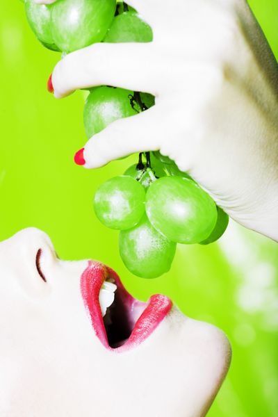 پرتره زن زیبا با آرایش رنگارنگ و پس زمینه در حال خوردن انگور