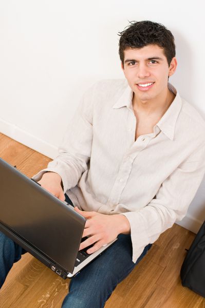 مرد جوان شادی که روی لپ تاپ خود با لباس های معمولی کار می کند