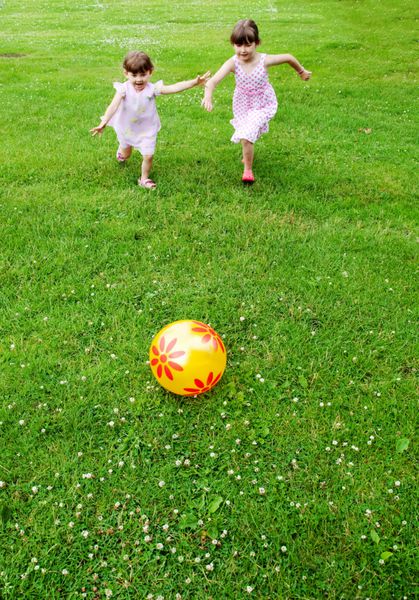 دو دختر رقابتی که به سمت توپ می دوند پس زمینه چمن سبز زمان تابستان