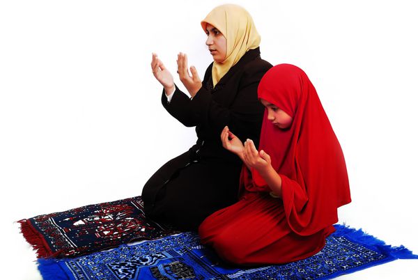 دختر جوان مسلمان با لباس سنتی در حال نماز خواندن با دختر کوچک