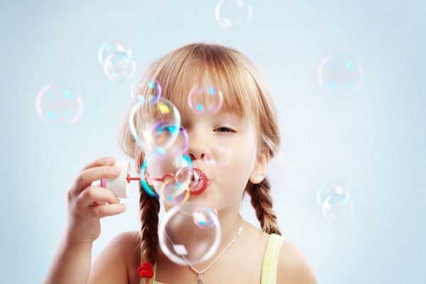 پرتره دختر کوچک دوست داشتنی بامزه ای که حباب های صابون را باد می کند