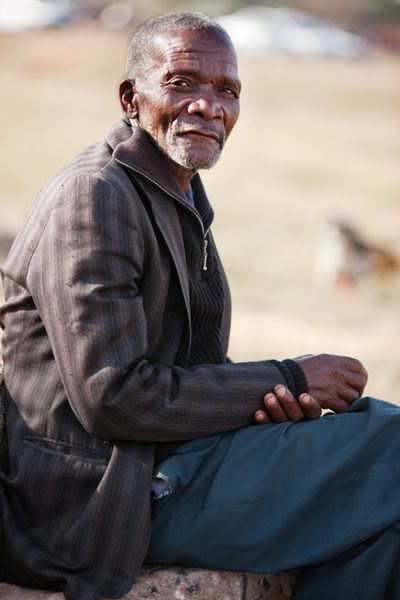 پیرمرد آفریقایی که روی پس‌زمینه صحرای آفریقایی تار و سنگی قرار گرفته است
