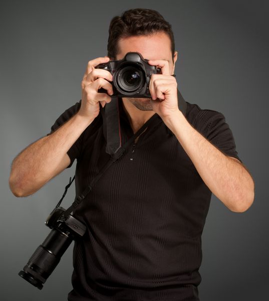 مرد سیاهپوش با دوربینش با دوربین اضافی که از بند آویزان است عکس می‌گیرد