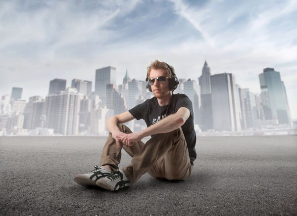 مرد جوانی با منظره شهری در پس‌زمینه نشسته و به موسیقی گوش می‌دهد