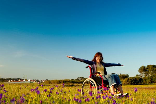 زن معلول شاد روی ویلچر بر فراز یک چمنزار سبز