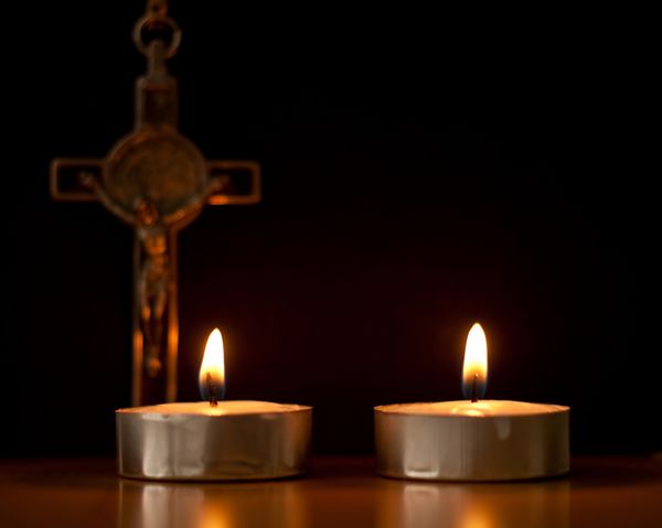 دو شمع چای روشن با صلیب در پس زمینه