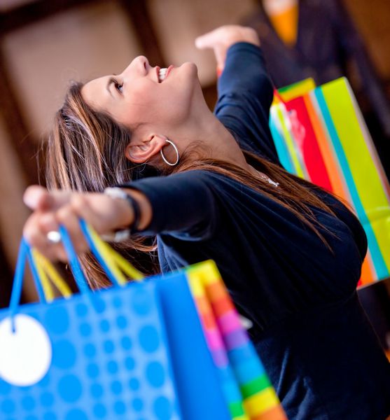 زن شاد در یک مرکز خرید که کیف‌هایی با آغوش باز نگه داشته است