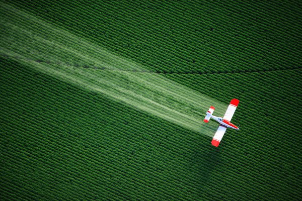 نمای هوایی از غبارپاشی محصول در حال پاشیدن در حالی که در ارتفاع پایین بر فراز مزارع مزرعه پرواز می کند