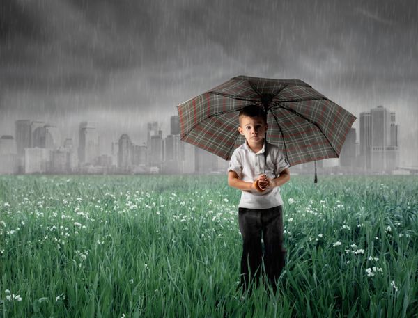 کودکی که زیر چتر روی یک چمنزار سبز با آسمان طوفانی در پس زمینه ایستاده است