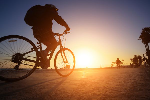 سیلوئت دوچرخه سواری که در امتداد ساحل در غروب آفتاب سوار می شود