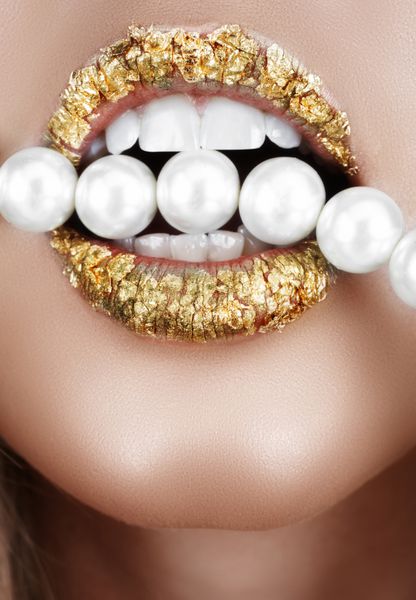 زنی با دهان باز با آرایش ورق طلا و دندان در حال گاز گرفتن مرواریدهای مصنوعی
