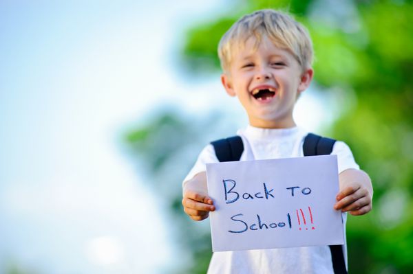 پسر جوان تابلوی دست نوشته بازگشت به مدرسه را در دست گرفته است