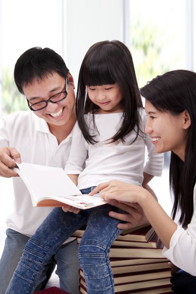 خانواده آسیایی خوشبخت در حال تحصیل با هم کمک والدین به دختر در خواندن کتاب