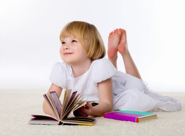 دختر کوچک روی زمین در حال مطالعه با کتاب و کاغذ