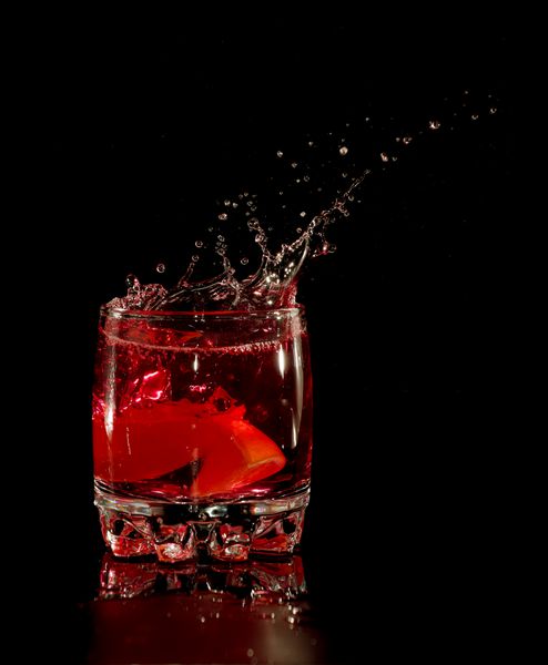 پاشیدن کوکتل مارتینی قرمز به شیشه در پس زمینه سیاه