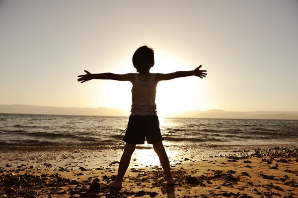شبح کودک در ساحل دستانش را بالا گرفته و خورشید را در آغوش گرفته است