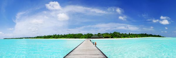 بهشت گرمسیری مالدیو - اسکله ای منتهی به یک جزیره مرجانی استوایی زیبا که در اقیانوس نیلگون هند پنهان شده است عکس پانوراما گسترده
