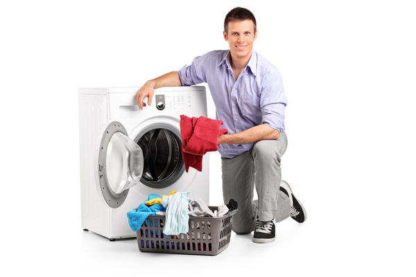 مرد جوانی که لباس‌ها را داخل ماشین لباسشویی می‌گذارد و روی پس‌زمینه سفید جدا شده لبخند می‌زند