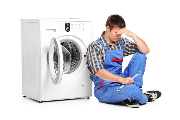 یک تعمیرکار ناامید در حال ژست گرفتن در کنار ماشین لباسشویی ایزوله شده در پس زمینه سفید