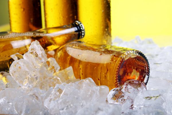 بطری های آبجو سرد و تازه با یخ روی پس زمینه زرد