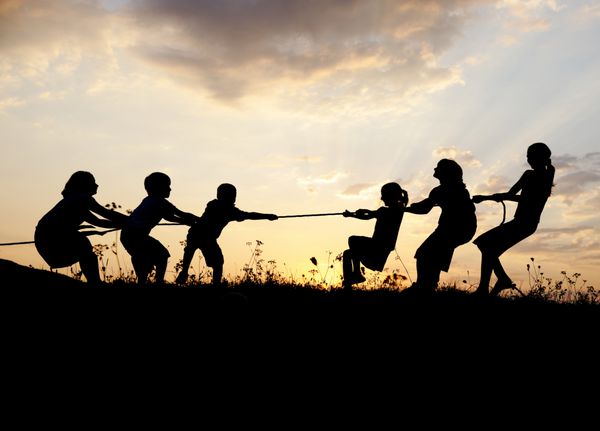 گروهی از کودکان شاد در حال بازی طناب کشی در چمنزار غروب آفتاب تابستان