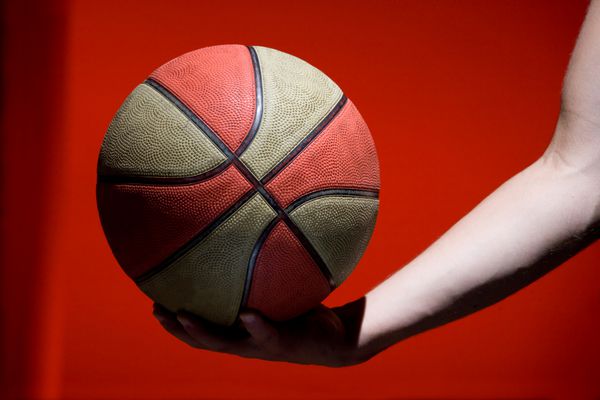 توپ بسکتبال در دست جدا شده در پس زمینه قرمز