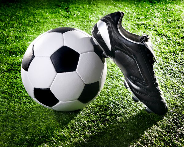 توپ فوتبال و کفش روی یک چمن سبز