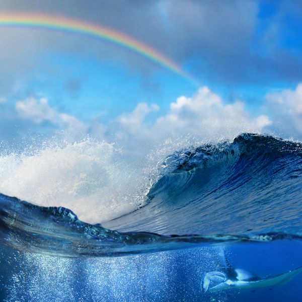 نمای اقیانوس تقسیم شده در سمت زیر آب با مانتارای احاطه شده توسط حباب های هوا و ساحل موج های بزرگ را با رنگین کمان رنگی می شکند