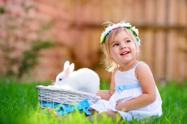 دختر کوچولوی ناز با خرگوش خرگوش عید پاک در پس زمینه چمن سبز دارد