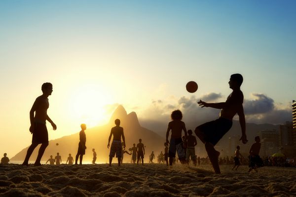 سیلوئت های غروب خورشید در حال بازی آلتینیو فوتبول فوتبال ساحلی با ضربه زدن توپ فوتبال ایپانما ساحل ریودوژانیرو برزیل
