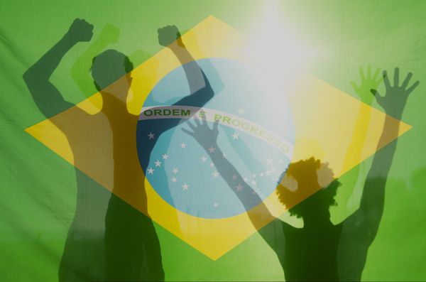 سایه‌های سایه‌ای برزیلی‌ها که در مقابل پرچم برزیل در نور شدید خورشید جشن می‌گیرند