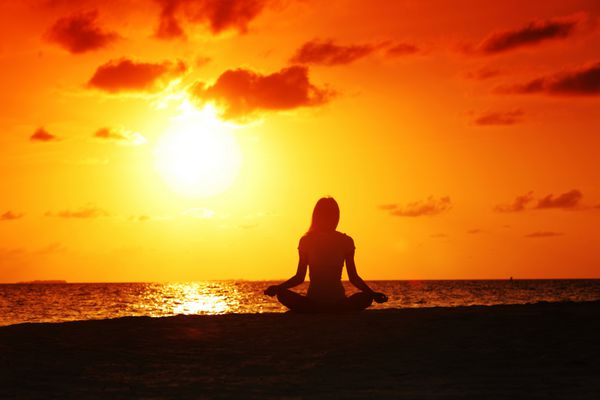 زن یوگا غروب خورشید در ساحل دریا