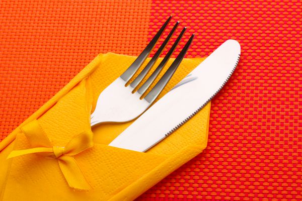 چنگال و چاقو در یک پارچه زرد با یک کمان روی یک سفره قرمز