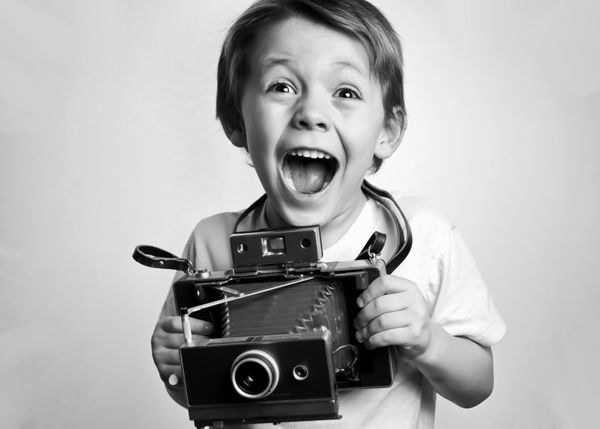 کودک خردسالی که یک دوربین فوری در پس زمینه سفید در دست دارد