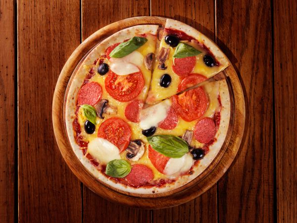پیتزا با ژامبون فلفل و زیتون روی تخته چوبی