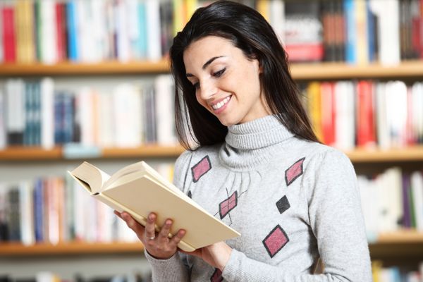 دانشجوی دختر خندان با کتاب در دست در کتابفروشی