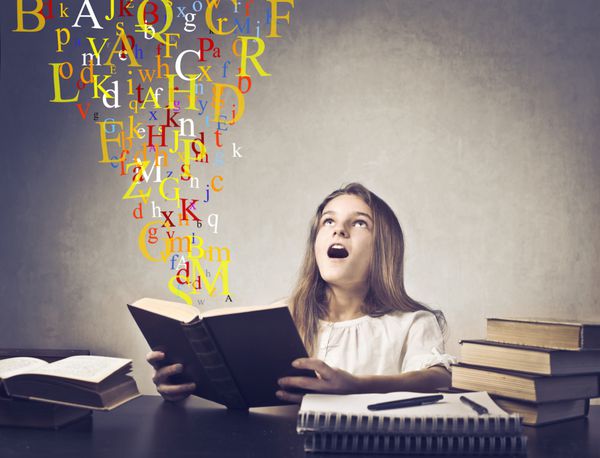 دختر نوجوان حیرت زده در حال خواندن کتابی با حروف الفبا که از روی آن پرواز می کند