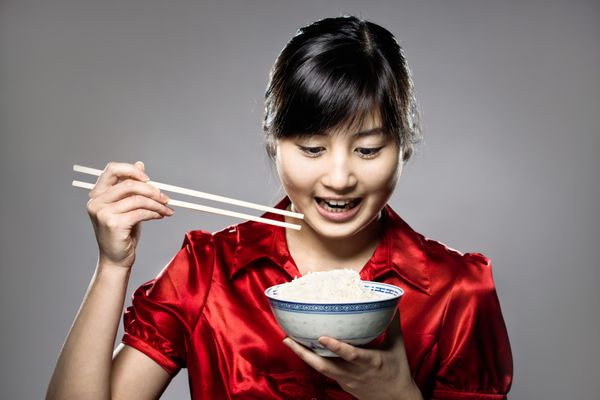 یک دختر جوان شاد آسیایی در حال خوردن برنج با کاسه و چاپستیک