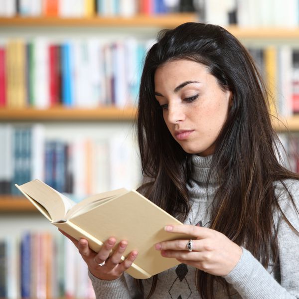 دانش آموز دختر در حال خواندن کتاب در کتابخانه