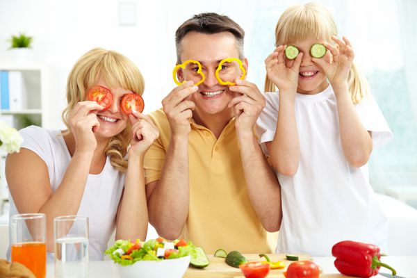 خانواده شاد در حال بازی با سبزیجات در آشپزخانه غذای سالم