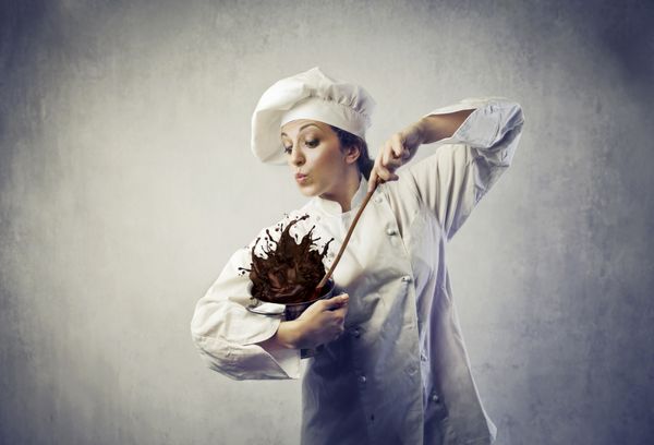 آشپز زن بامزه در حال مخلوط کردن مقداری خمیر شکلاتی که از یک قابلمه می ریزد