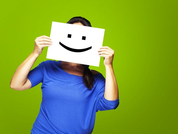 زن در حال نشان دادن شکلک شاد در مقابل صورت در پس زمینه سبز