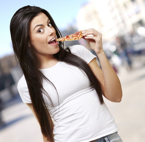 زن جوان در حال خوردن یک تکه پیتزا در پس زمینه خیابان