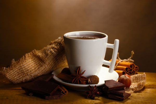 فنجان شکلات داغ چوب دارچین آجیل و شکلات روی میز چوبی در زمینه قهوه ای