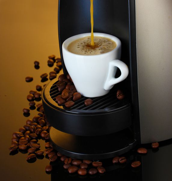 دستگاه اسپرسو در حال ریختن قهوه در فنجان در زمینه قهوه ای